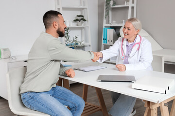 Obraz premium Female doctor with young man shaking hands at table in clinic