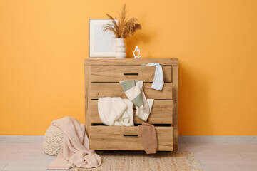 Commode with scattered clothes near yellow wall in living room