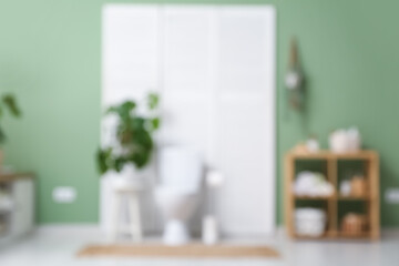 Interior of restroom with toilet bowl, folding screen and shelving unit near green wall. Blurred view
