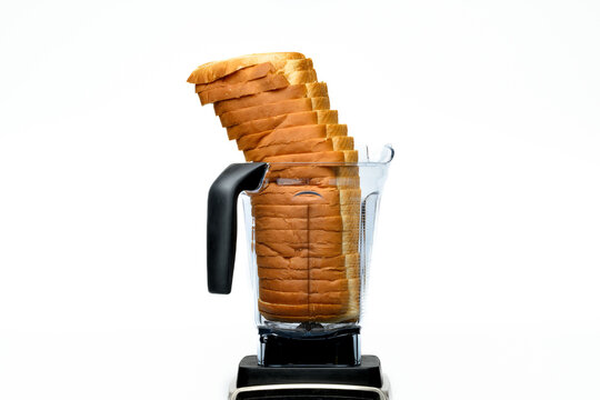 A leaning loaf of sliced bread in a clear plastic blender against a white backdrop