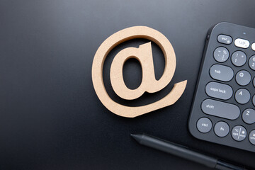 Wooden e-mail address sign with computer keyboard, pen, and copy space, top view on the black...