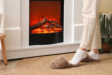 Woman putting on soft slippers near fireplace at home