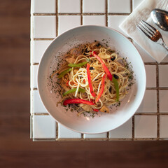 A delightful bowl of spaghetti featuring colorful bell peppers and a sprinkle of herbs placed on a...
