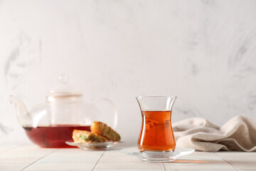 Glass of Turkish tea with teapot and tasty baklava on white tile table