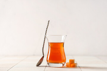 Glass of Turkish tea with spoon and sugar cubes on white tile table