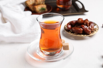 Glass of Turkish tea with dried dates and sugar cubes on white background