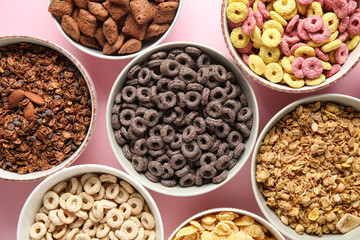Bowls with different cornflakes on pink background