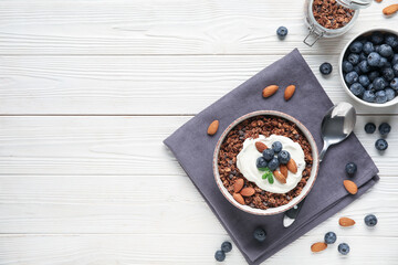 Bowl with chocolate tasty granola, yogurt, nuts and berries on white wooden background