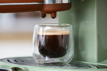 Modern coffee machine with glass of hot espresso in kitchen, closeup