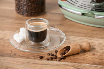 Glass of hot espresso with beans and modern coffee machine on wooden background