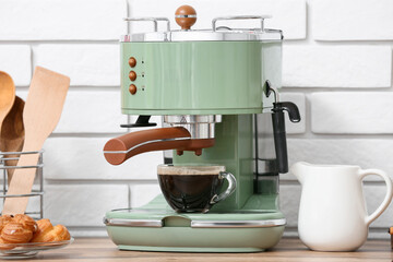Modern coffee machine with glass cup of hot espresso and plate of sweet cakes on wooden table near...