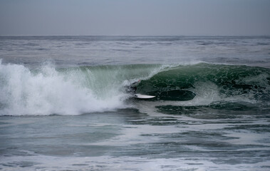 Surfer in wetsuit and surfboard riding large wave