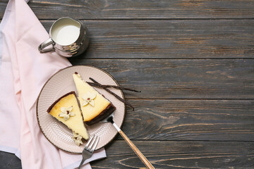 Plate with pieces of sweet vanilla cheesecake and jug of milk on black wooden background
