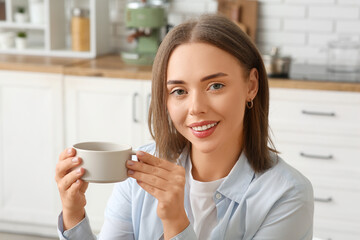 Beautiful young woman with cup of hot coffee in kitchen