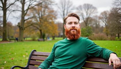 Fototapeta premium Content man with red beard sitting on park bench, relaxation concept