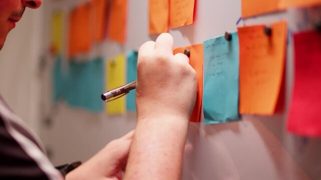 Focused man writes on a sticky note, planning and brainstorming in office setting.