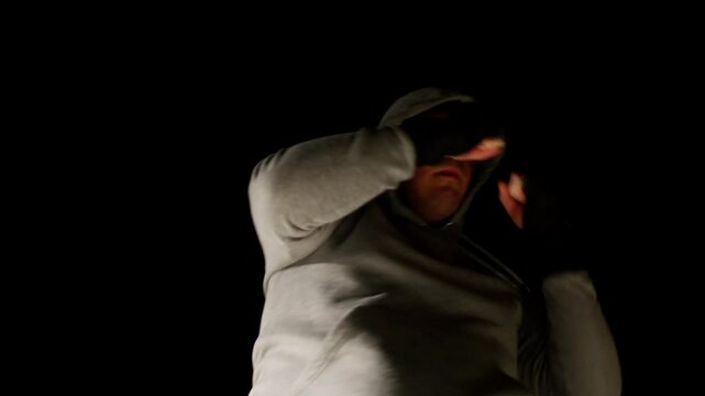 Low-angle shot of a man in a hoodie shadowboxing under dramatic lighting.
