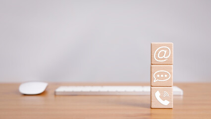 Cube wood block stacked on wooden table with phone, message bubble, and email sign icon with...