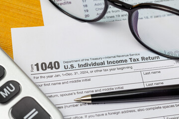 Tax form 1040 with calculator, glasses and pen on wooden table, close up