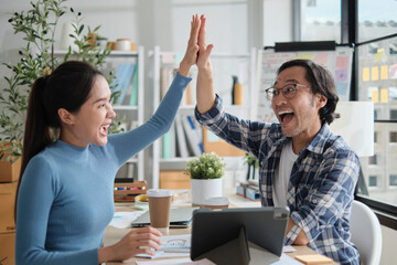 Two Asian startup entrepreneurs partner cheerful and high five together, successful marketing jobs...