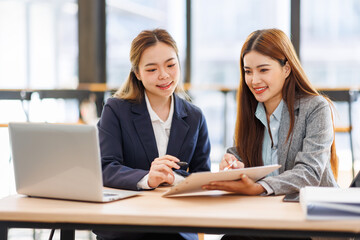 Two asian women analyzing documents while sitting on a laptop screen in office. Woman executives at work in office discussing some paperwork.