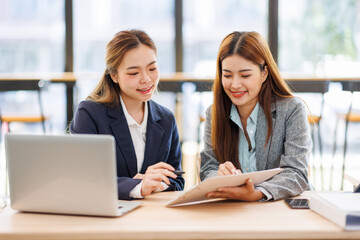 Two asian women analyzing documents while sitting on a laptop screen in office. Woman executives at work in office discussing some paperwork.