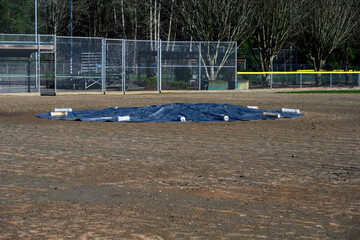 Baseball diamond with the pitcher’s mound covered and protected for winter by a black tarp...