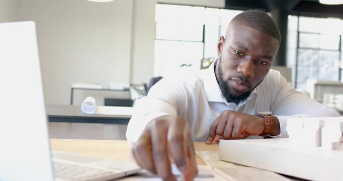 Using protractor, African American businessman measuring and working on architectural model in offic
