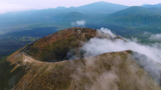 Pan-left aerial view of Paricutin Volcano crater with a road encircling the summit, partially veiled by mystical clouds in Michoac&aacute;n, Mexico