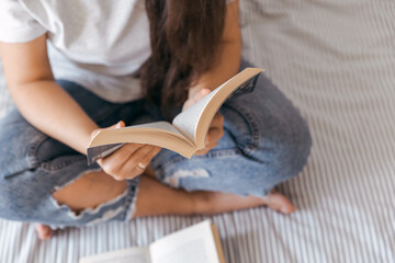 Young girl with brown hair is reading a book in a room. Top view