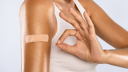 Successful Covid-19 Vaccination. Closeup Cropped View Of Vaccinated Woman Gesturing Okay Sign And Showing Arm With Adhesive Bandage After Getting Corona Virus Vaccine Injection, Isolated, Banner