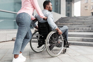 Obraz premium Problems with accessible environment for people with physical disability. Young black woman with millennial man in wheelchair having no possibility to enter building without ramp, outdoors