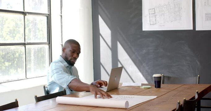 Architect working on blueprints and using laptop in modern office
