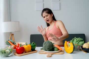 Young woman rejecting healthy food, making a disgust expression in her modern and bright apartment