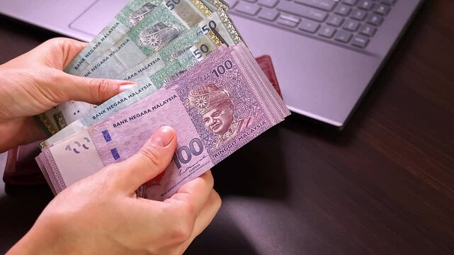 Close up view of business woman calculating salary money paper banknotes (Malaysian ringgit MYR), managing monthly budget payment, exchange finance currency at office workplace. Laptop in background.