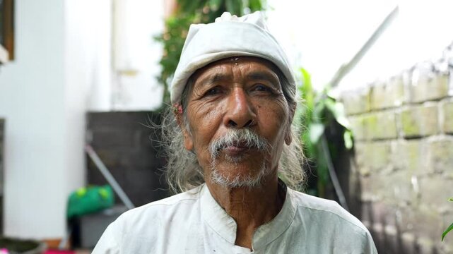 Portrait elderly man smile with a serene expression wearing a traditional white outfit and head covering, standing outdoors. Old man look at camera. His wrinkled face reflects wisdom and experience.