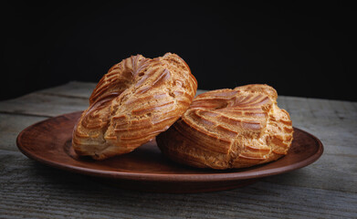 A clay plate with profiteroles stands on a wooden surface. Profiterole cake. Eclair in the form of a ring.