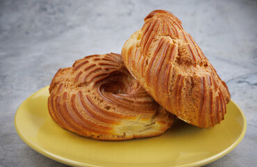 Two profiteroles lie in a yellow plate. The eclair is in the shape of a ring.