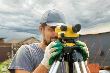 Obraz premium young man working as a geodetic leveler during construction of a new private house on a sunny summer day