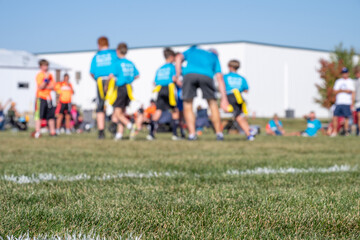 Selective focus on flag football grass with blurred youth team huddle in the background