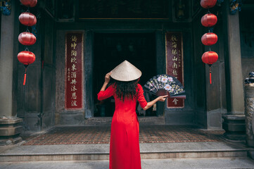 A woman in a traditional Vietnamese costume, a conical hat with a fan in her hands against the...