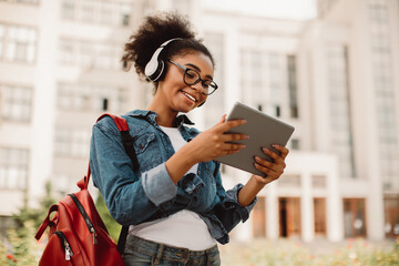 E-Learning. Happy Black Female Student Using Tablet Computer Wearing Headphones Standing Near...