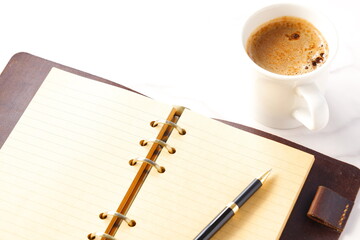 ミルクをたっぷり入れたコーヒー、カフェ・ラッテを飲みながら、システム手帳でデスクワーク中のイメージ
