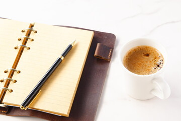 ミルクをたっぷり入れたコーヒー、カフェ・ラッテを飲みながら、システム手帳でデスクワーク中のイメージ
