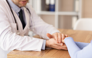 Medical Ethics Concept. Friendly male doctor holding female patient's hands for encouragement and...