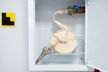 Fire hose in storage cabinet ready for emergency use with safety markings nearby