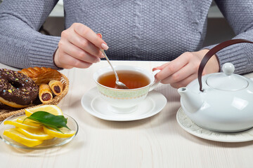 Woman in a sweater, holding a cup of hot tea. Hands close-up.