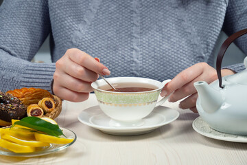 Woman in a sweater, holding a cup of hot tea. Hands close-up.