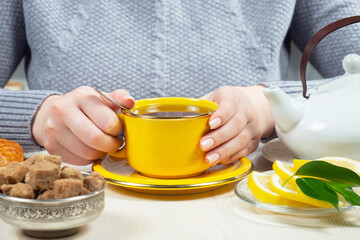 Woman in a sweater, holding a cup of hot tea. Hands close-up.