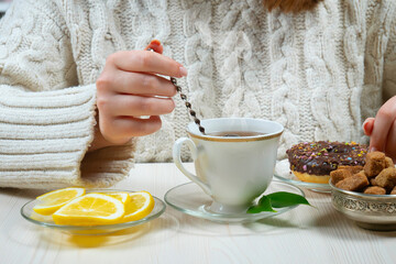 A woman in a large knit sweater holds a cup of hot tea in her hands. Hands close-up.